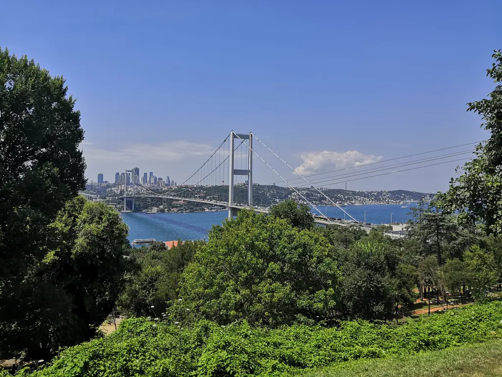Mihrabat Tabiat Parkı'ndan Boğaz; önde yamaçtaki yeşil ağaçlar, ortada Fatih Sultan Mehmet Köprüsü, ötesinde Levent'in kuleleri ve mavi gökyüzü.