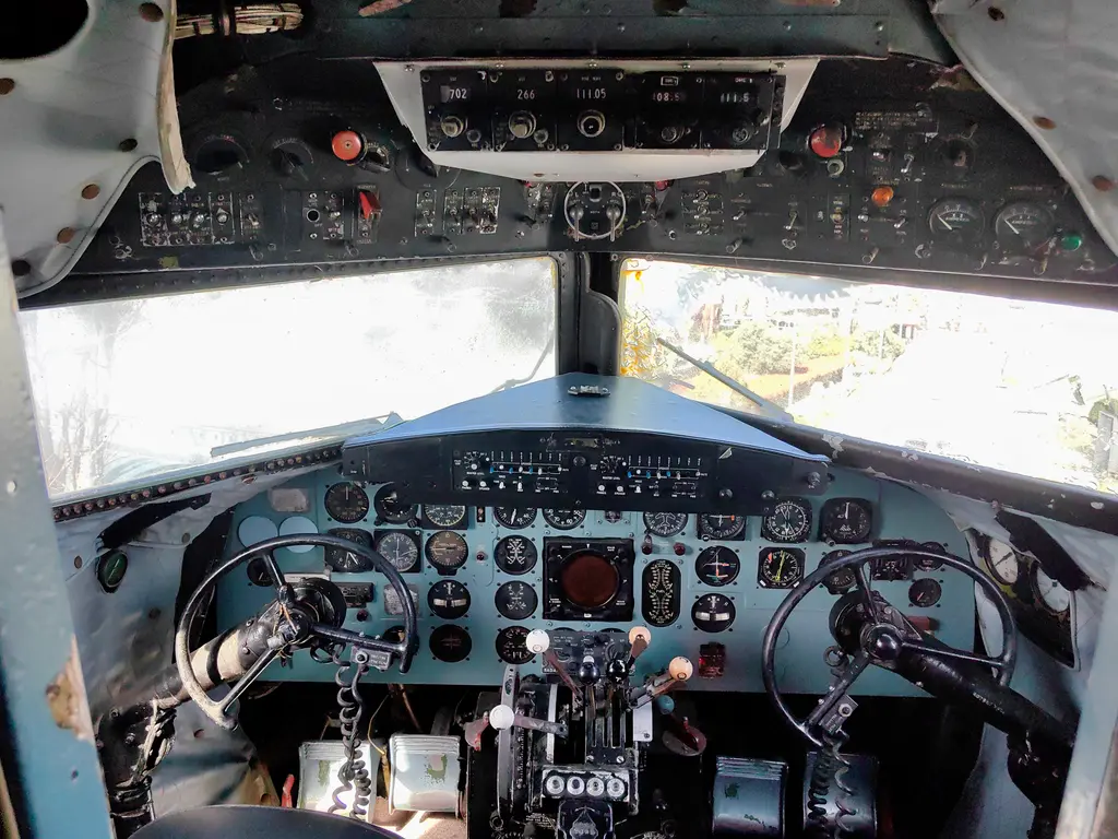 Douglas DC-3 uçağının kokpiti; iki pilot koltuğu, kumanda kolları, kadranlarla dolu gösterge panosu ve ön camlar.