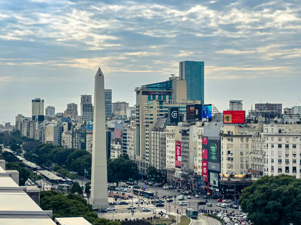 Arjantin'de Buenos Aires'in kuş bakışı silüeti; ünlü Obelisco anıtı, geniş 9 de Julio Bulvarı ve ağaçlı caddeleri saran gökdelenler, bulutlu gökyüzü altında.