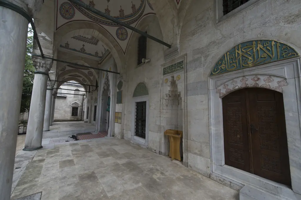 Nişancı Mehmed Paşa Camii'nin avlusundan revaklar; sivri kemerler, mermer sütun başlıkları, ahşap kapılar ve yeşil zeminli yazı levhası.