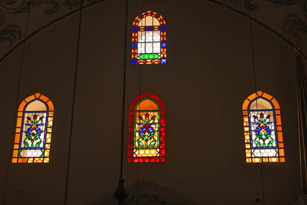 Mahmut Paşa Camii'nde renkli camlı pencereler; loş duvarda kırmızı, sarı ve mavi camlarla lale ve çiçek desenli dört sivri kemerli pencere.