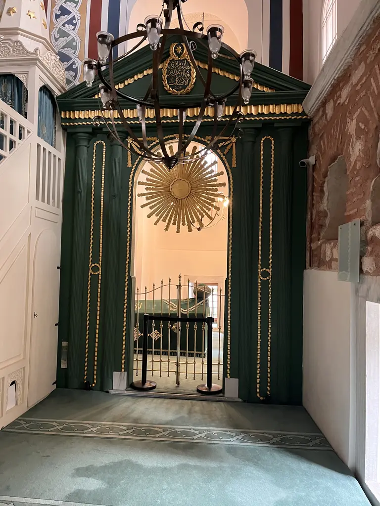 Atik Mustafa Paşa Camii'nde Hz. Câbir makamının girişi; koyu yeşil ve altın yaldızlı ahşap çerçeve, üstte hat levhası ve yaldızlı Mahmud güneşi, içeride demir parmaklık.