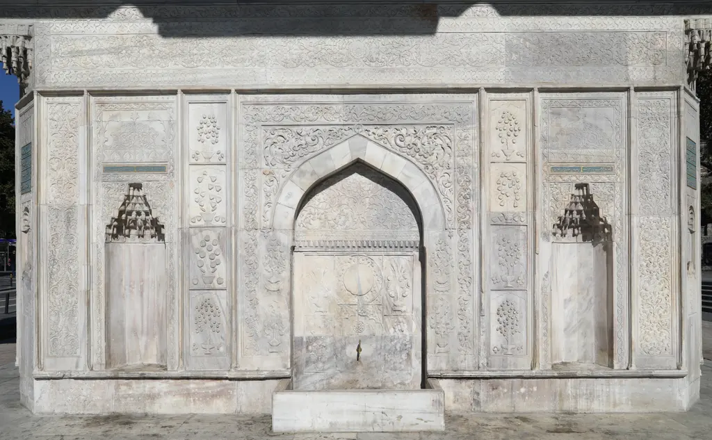Tophane Çeşmesi'nin bir cephesi yakından; sivri kemerli orta niş, mukarnaslı yan nişler ve mermer yüzeyi dolduran bitkisel kabartmalar.