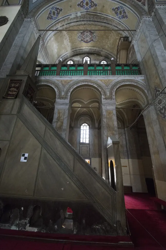 Gül Camii'nin minberi; mermer taklidi boyalı ahşap gövde ve merdiven, arkasında yan nef kemerleri, yeşil korkuluklu galeri ve kırmızı halı.