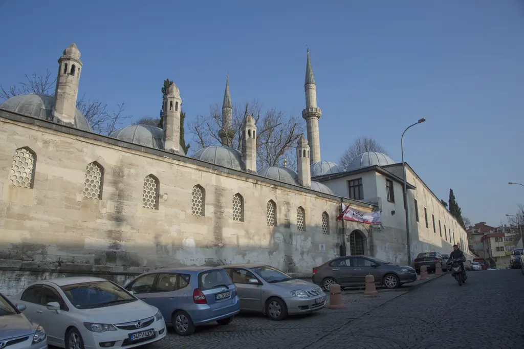 Atik Valide Külliyesi; sokak boyunca uzanan kesme taş duvar, kubbeler, ocak bacaları ve minareler.