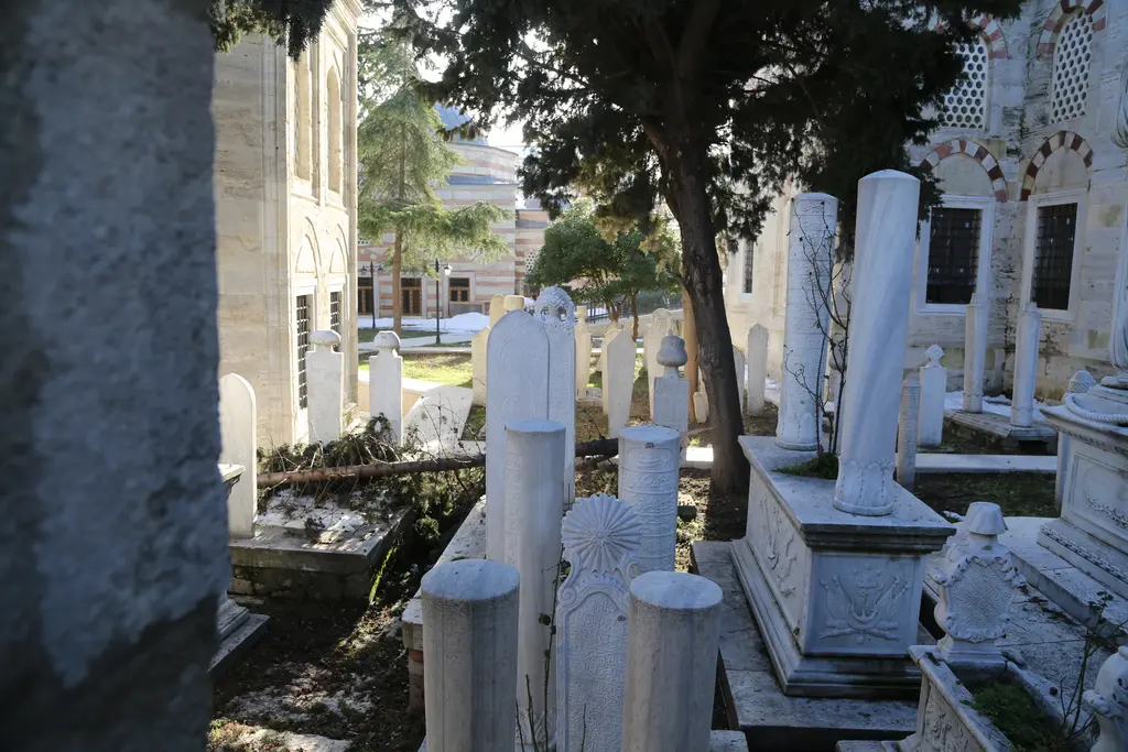 Kılıç Ali Paşa Camii'nin haziresi; ağaçların altında sıralanan beyaz mermer mezar taşları, sarıklı ve sütun biçimli şahideler ve lahitler.