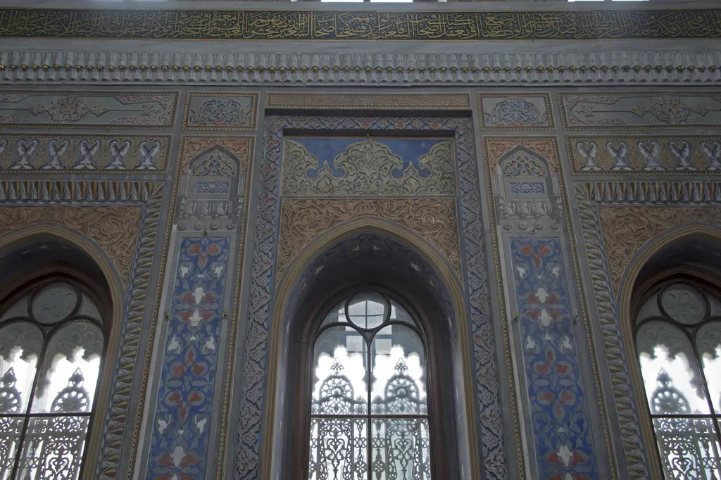 Pertevniyal Valide Sultan Camii'nde duvar süslemeleri; mavi ve altın kalem işi paneller, sivri kemerli pencereler ve mermer şebekeler.