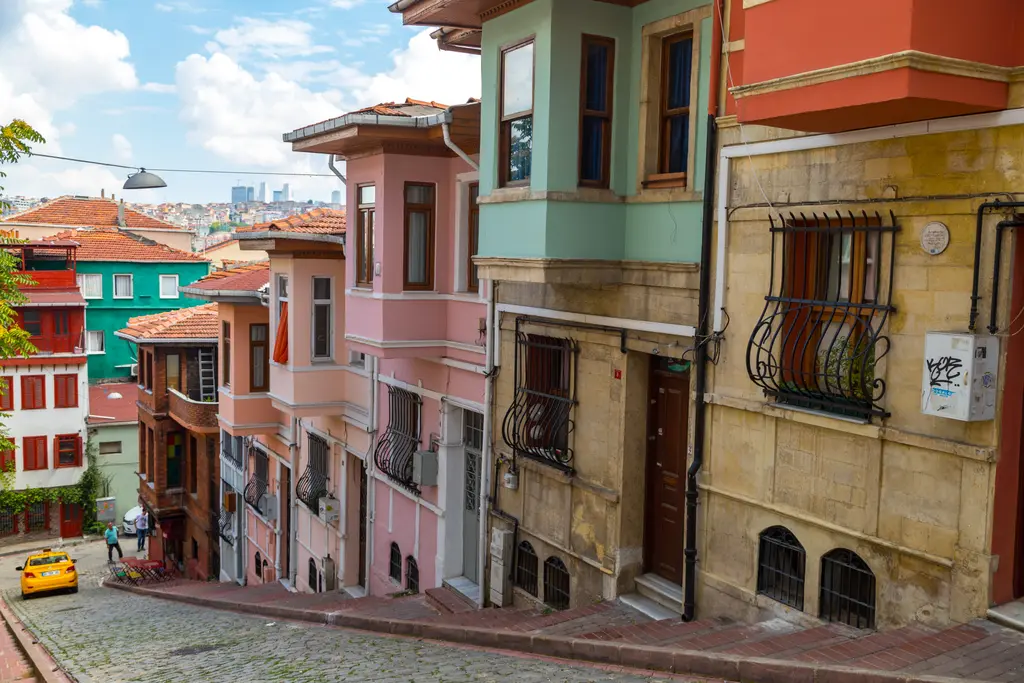 Balat'ta aşağı inen yokuş sokak; pembe, yeşil ve sarı evler, cumbalar, arnavut kaldırımı ve uzakta Haliç.