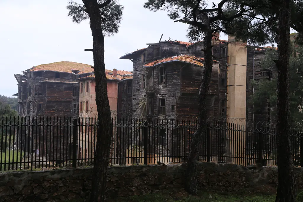 Büyükada Rum Yetimhanesi; demir çitin ardında tuğla baca, ahşap kanatlar ve çam ağaçları.