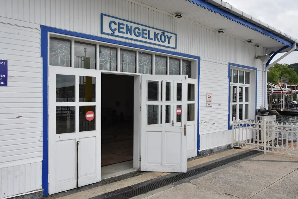 Çengelköy İskelesi'nin girişi; beyaz ahşap kapılar, mavi çerçeveli camlar ve üstte Çengelköy yazılı tabela.