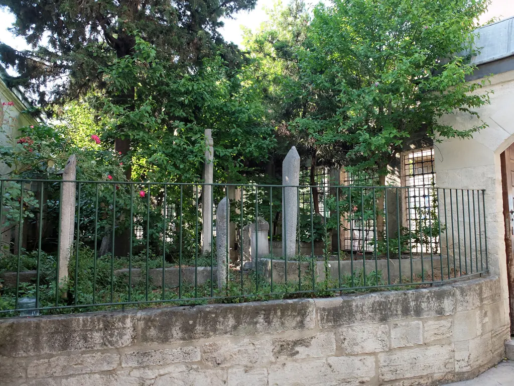 Nişancı Mehmed Paşa Camii'nin haziresinde ağaçlar altında sarıklı mezar taşları, alçak taş duvar ve üstündeki yeşil demir parmaklık.