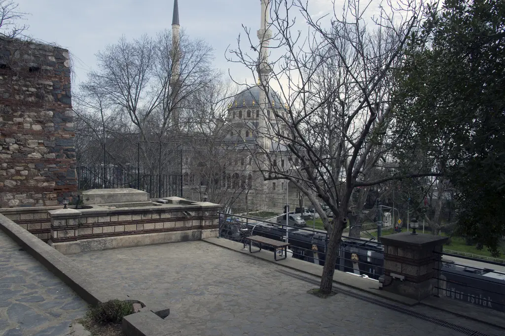 Tophane-i Âmire'nin doğu yanında taş döşeli avlu; yapraksız ağaçlar, alçak duvar ve arkada Nusretiye Camii'nin kubbesi.