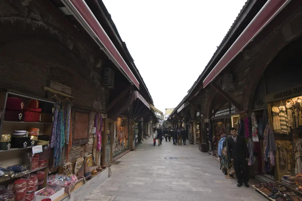 Arasta Çarşısı'nda karşılıklı iki sıra dükkân; tuğla kemerler, tenteler, önlerinde sergilenen tekstiller ve sokakta yürüyen insanlar.