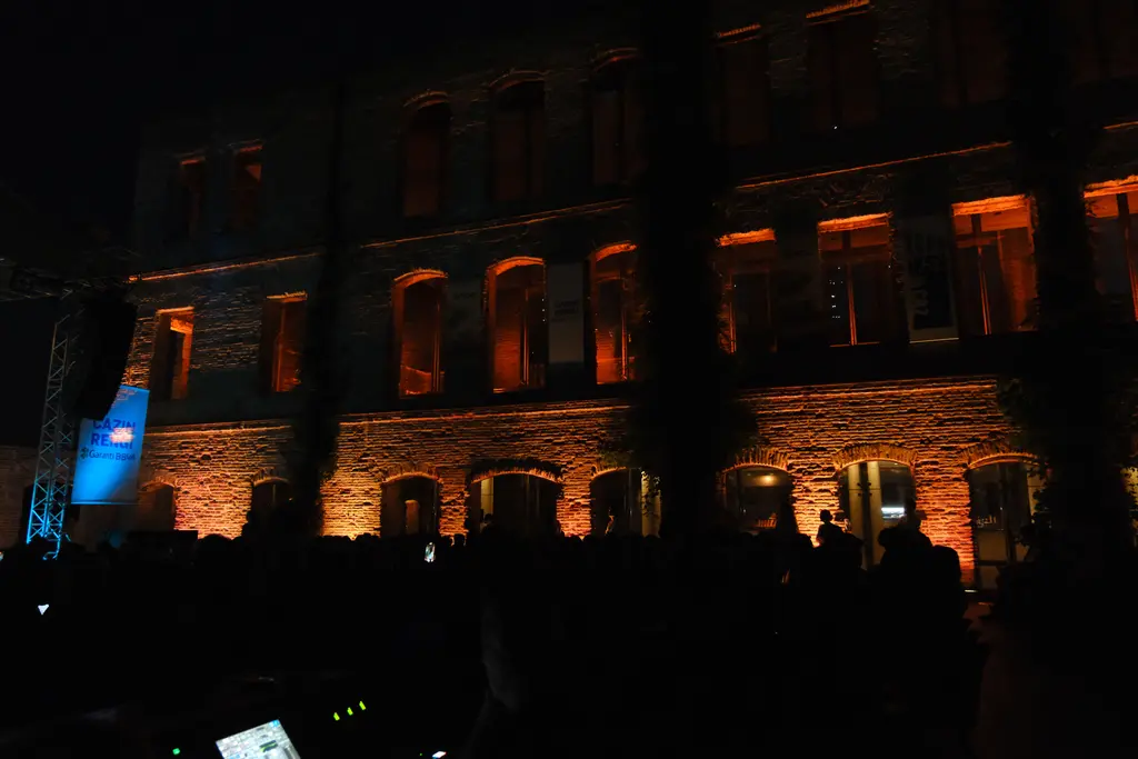 Esma Sultan Yalısı'nın bahçesinde konser akşamı; mavi sahne ışıkları, ışıklandırılmış tuğla duvarlar ve izleyiciler.