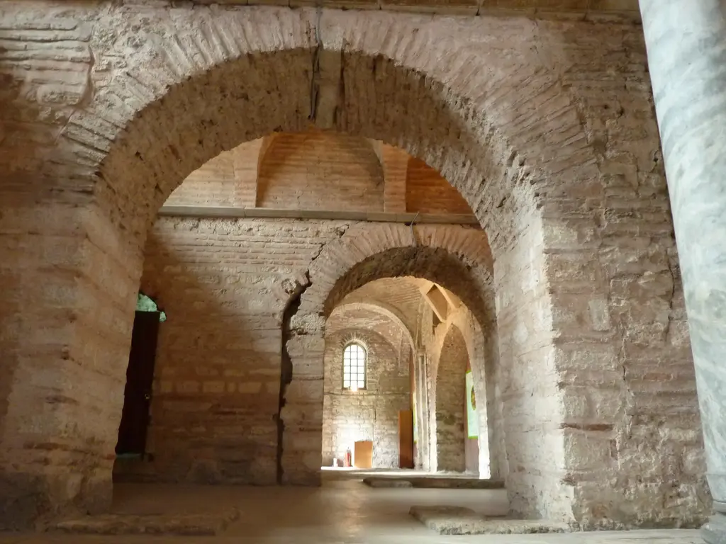 Fethiye Camii'nde sıvasız iç mekân; üst üste açılan tuğla kemerler, tonozlu tavan, uzaktaki kemerli pencere ve düz zemin.