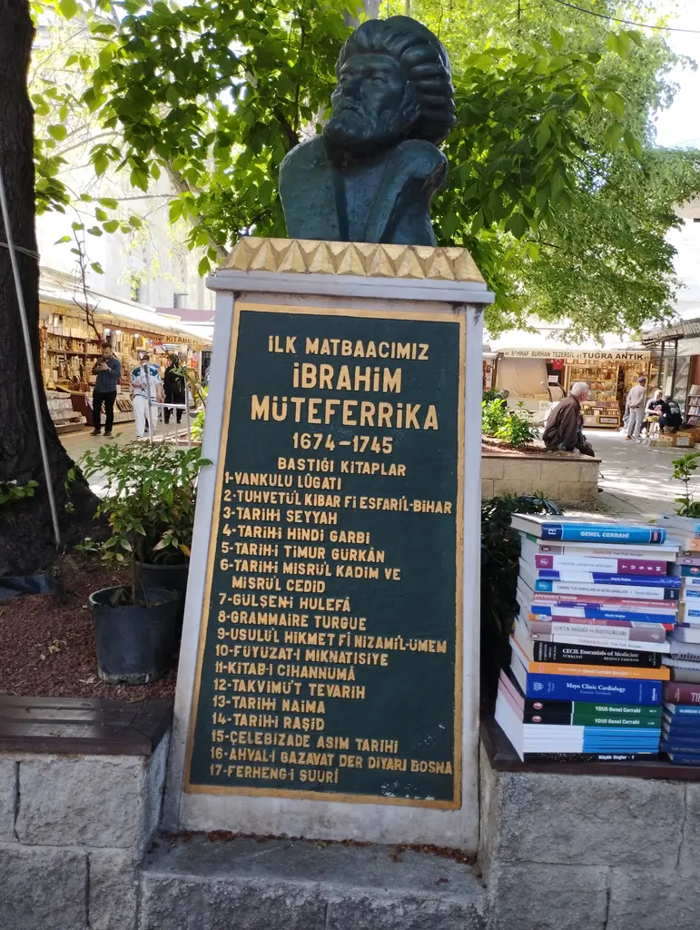 Sahaflar Çarşısı'nda Müteferrika anıtının kitabesi; beyaz mermer levhada "İlk matbaacımız İbrahim Müteferrika 1674-1745" satırı ve altında numaralanmış kitap listesi, sağ altta kitap yığınları.