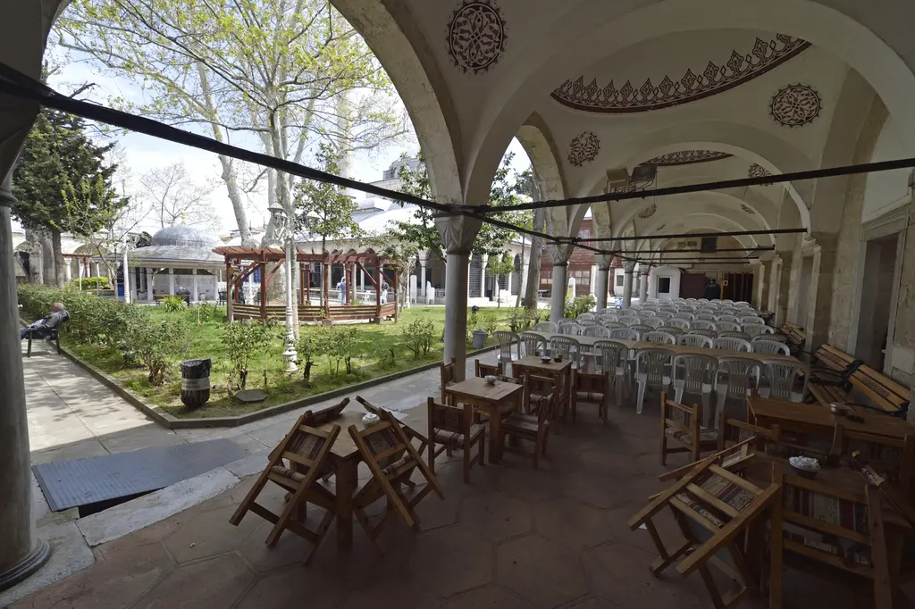 Üsküdar'da Atik Valide Camii'nin avlusu; revak altında ahşap masalar ve sandalyeler, ağaçlar ve şadırvan çevresi.