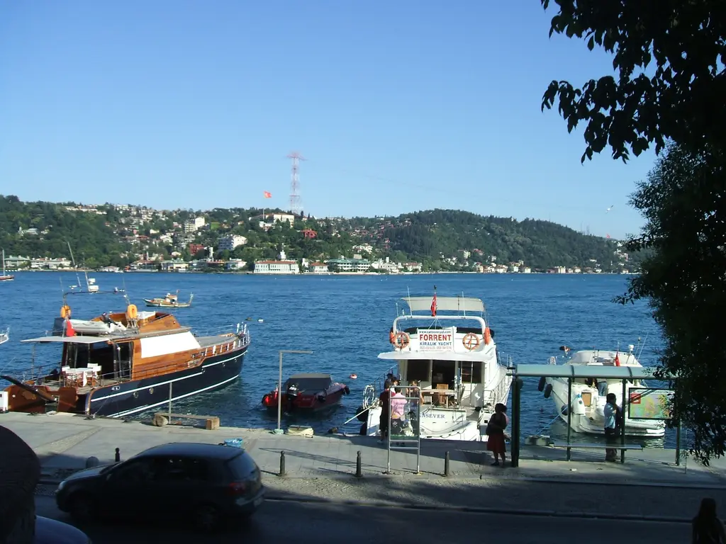 Bebek'te rıhtım; kıyıya bağlı ahşap gezi tekneleri, beyaz yat, durak ve karşıda Anadolu yakası.