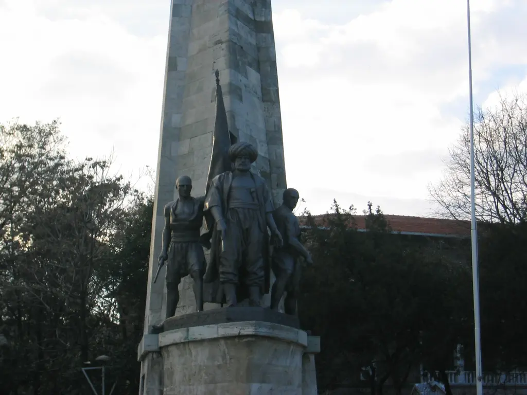 Barbaros Anıtı; ağaçların önünde yüksek taş kaide, bronz heykel grubu ve önündeki geniş meydan.
