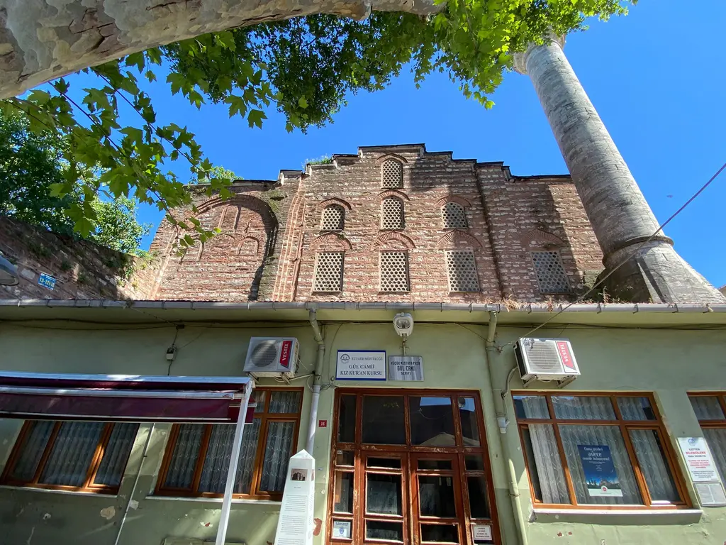 Gül Camii'nin giriş yapısı; açık yeşil boyalı alçak cephe, ahşap çift kanatlı kapı ve levhalar, üstte tuğla örgülü gövde, sağda minare.