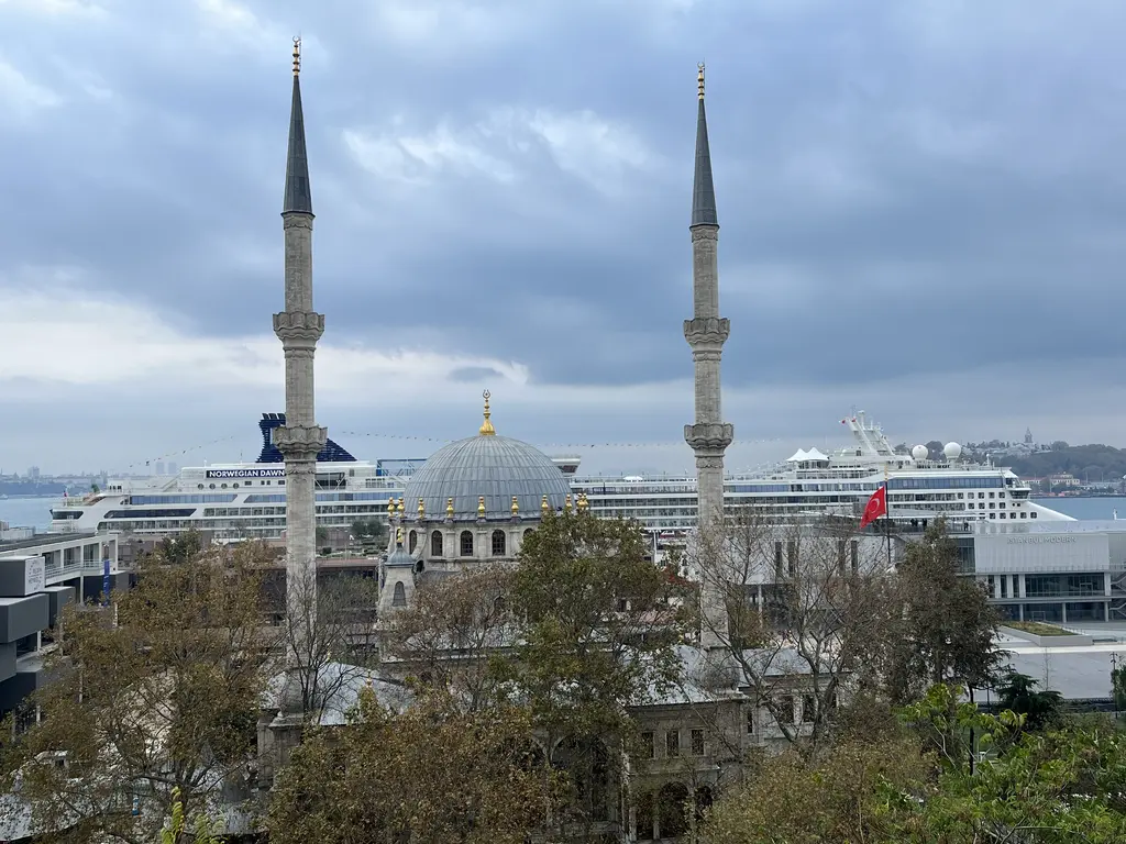 Nusretiye Camii'nin iki minaresi ve kubbesi; önde sonbahar renginde ağaçlar, arkada Galataport rıhtımına yanaşmış büyük bir yolcu gemisi.