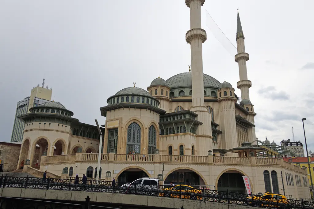 Taksim Camii'nin yan cephesi; kemerli alt kat, sıra sıra pencereler, kademeli kubbeler ve iki şerefeli ince minareler.