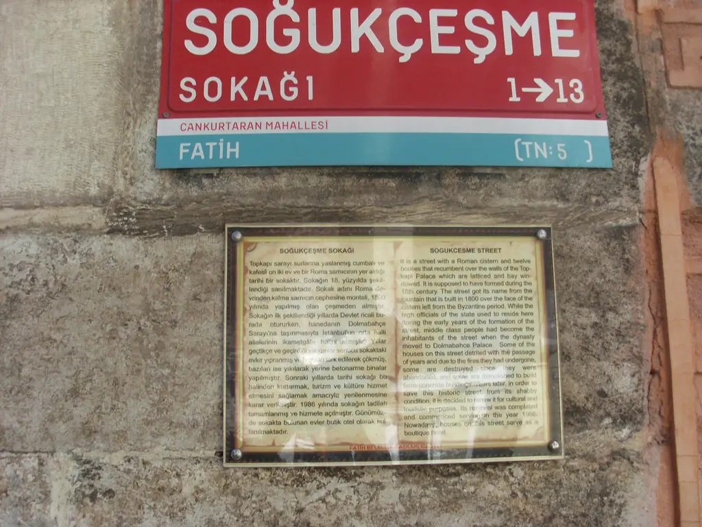 Soğukçeşme Sokağı'nın taş duvara asılı kırmızı sokak tabelası; altında sokağın tarihini anlatan iki dilli, çerçeveli bilgi levhası.