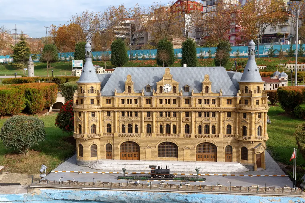 Miniatürk'te Haydarpaşa Garı maketi; sarı bej taş cephe, gri çatı, iki konik kule ve saat, önünde siyah bir buharlı lokomotif maketi.