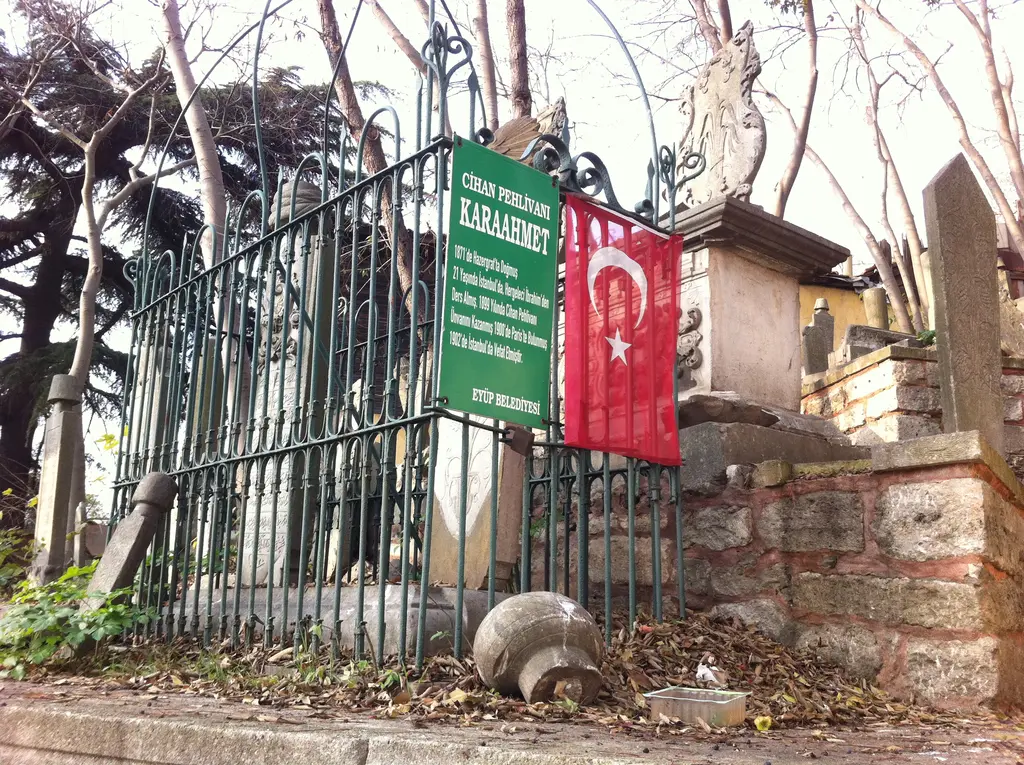 Eyüp Mezarlığı'nda Kara Ahmet'in kabri; demir parmaklıklı kabir, yeşil tabela, Türk bayrağı ve devrilmiş eski taşlar.