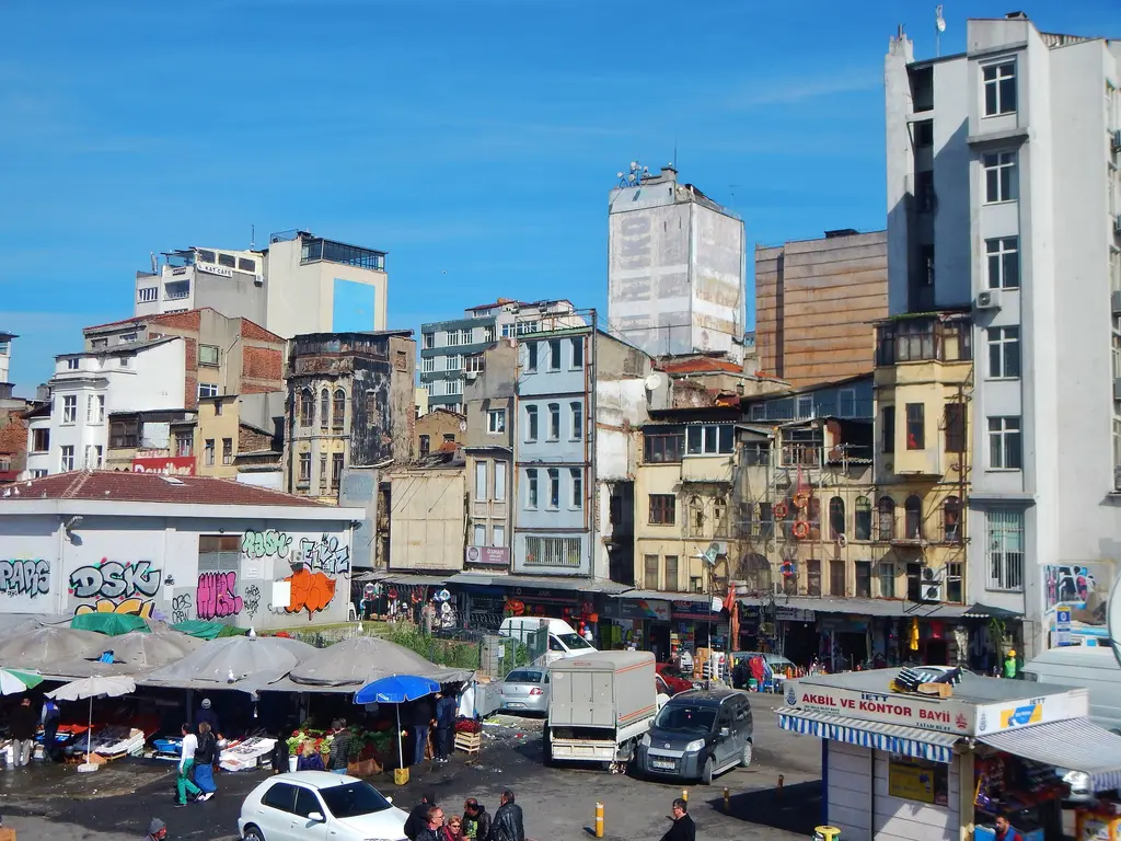 Karaköy'de bir açık pazar; şemsiyeli tezgâhlar, duvar yazılı bir yapı, park etmiş araçlar ve arkada eski binalar.