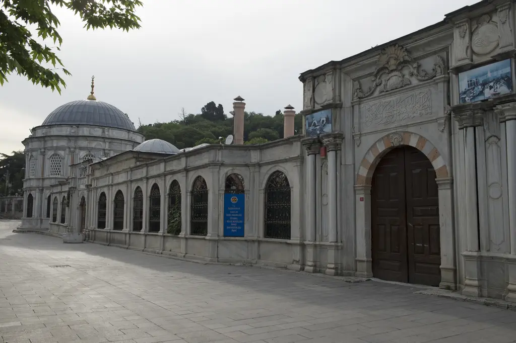 Mihrişah Valide Sultan Külliyesi'nin sokak cephesi; uzun mermer duvar, sıralı şebekeli pencereler, ahşap kanatlı taç kapı ve arkada türbenin kubbesi.