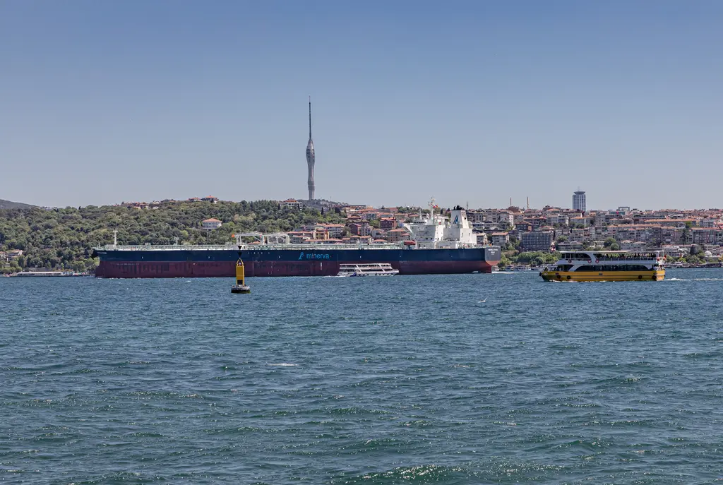 Boğaz'dan Üsküdar kıyısı; mavi su, kıyıda yanaşmış gemi, yamaçta yerleşim ve tepede ince Çamlıca Kulesi.