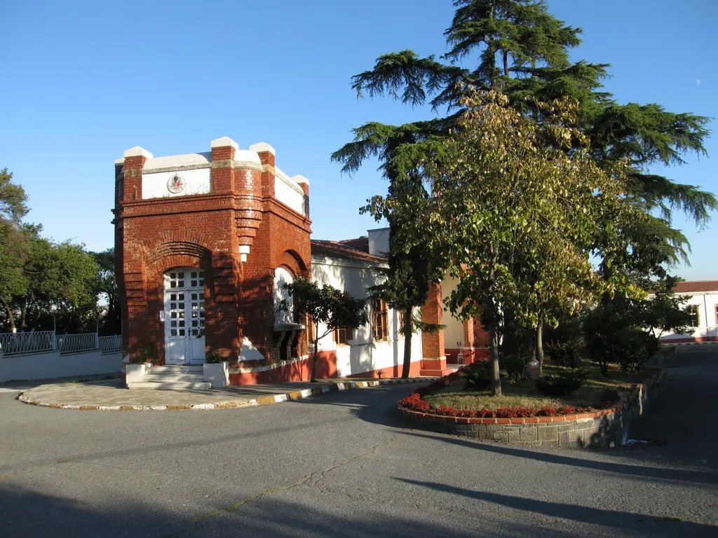 Yıldız Parkı'nda Yıldız Porselen Fabrikası; kırmızı tuğla kuleli yapı, önünde çiçekli göbek, yanında yüksek bir sedir ağacı.