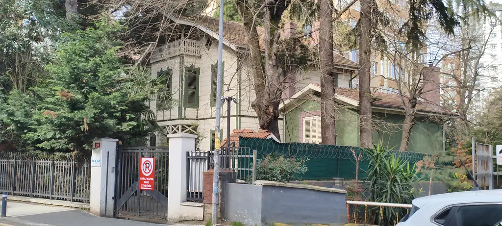 Göztepe'de Ömer Faik Paşa Köşkü; ağaçların arasında yeşil ahşap köşk, beyaz taş kapı direkleri ve demir parmaklık.