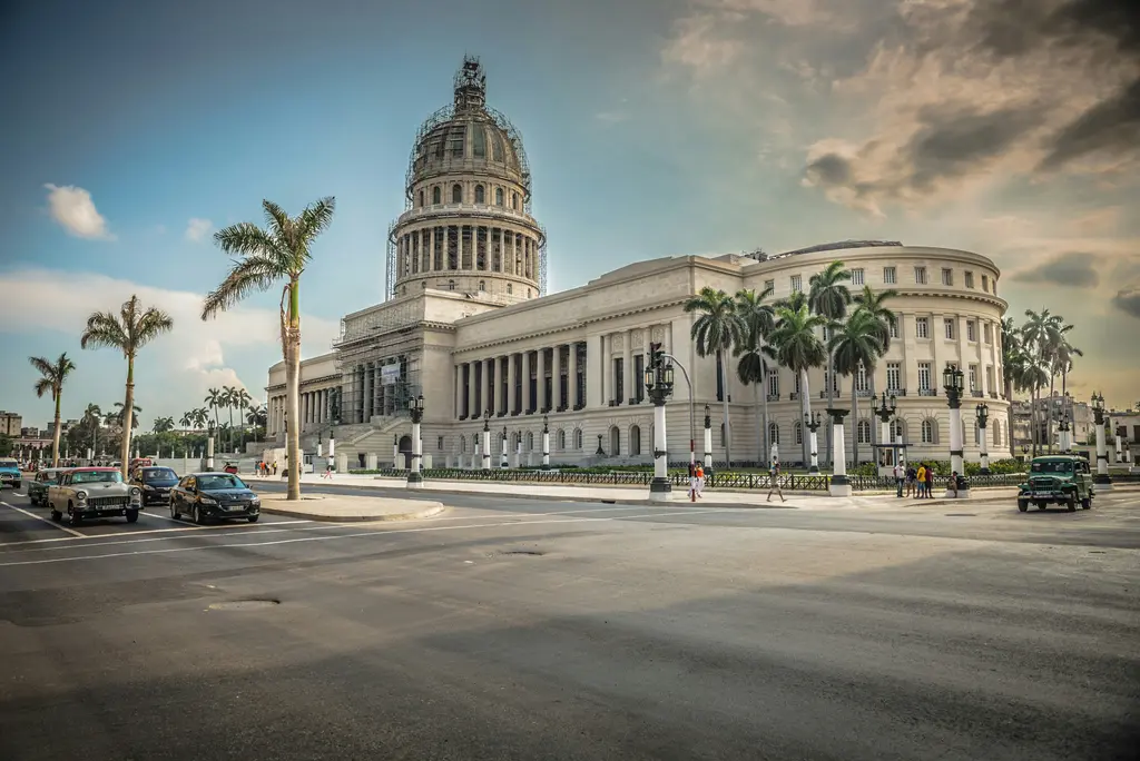 Havana'da El Capitolio binası; taş sütunlu anıtsal cephesi, ortada yükselen büyük kubbesi, önündeki palmiye sırası ve geniş cadde.