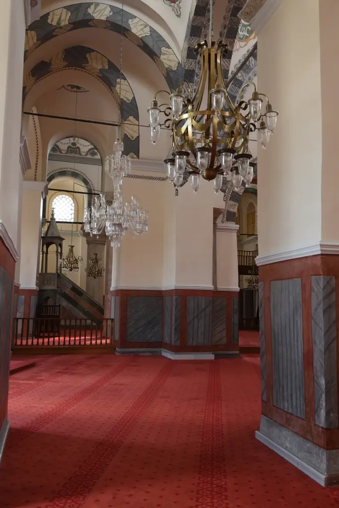 Zeyrek Camii'nin harimi; kırmızı desenli halı, yeşil yapraklı kalem işiyle bezenmiş kemerler, kristal ve pirinç avizeler, gri kırmızı mermer kaplı duvar altlığı.