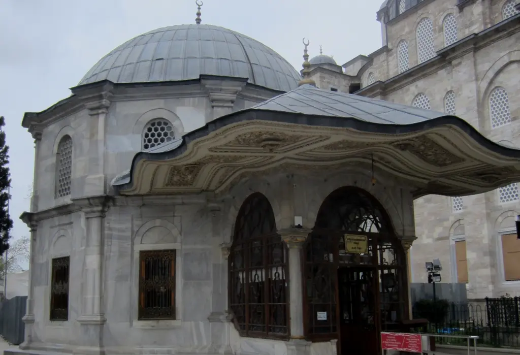 Fatih'te Fatih Sultan Mehmet Türbesi; sekizgen beyaz mermer gövde, kurşun kubbe ile altın alem, girişin üzerine uzanan dalgalı barok taş saçak ve camekânlı kapı.