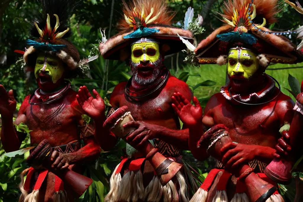 Papua Yeni Gine'de geleneksel sing-sing gösterisinde üç kabile erkeği; sarı yüz boyaları, kırmızıya boyanmış gövdeleri, tüylü başlıkları ve ellerinde davullarıyla.