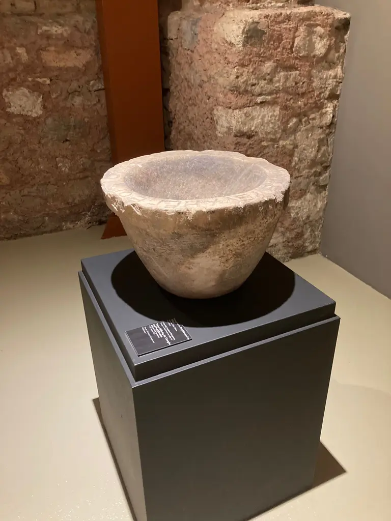Georgios ve Polykhronios'un Adağı; siyah kaide üstünde kalın kenarlı mermer tekne, arkada tuğla duvar ve açık renkli zemin.
