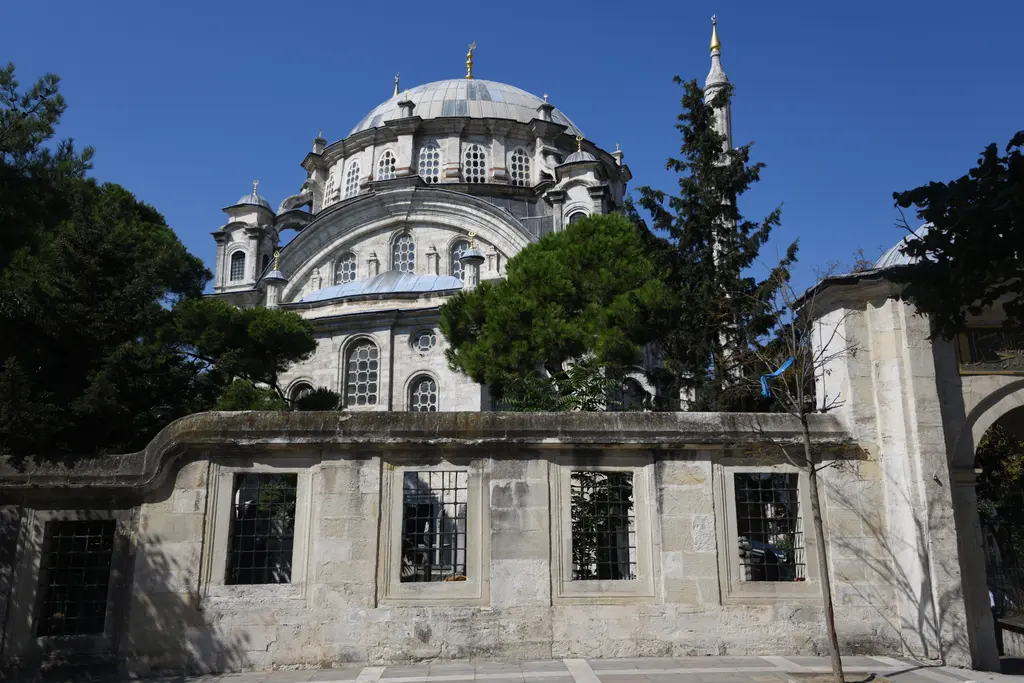 Selimiye Camii'nin kubbesi; avlu duvarının ardında kurşun kubbe, pencereli kasnak, ağaçlar ve mavi gökyüzü.