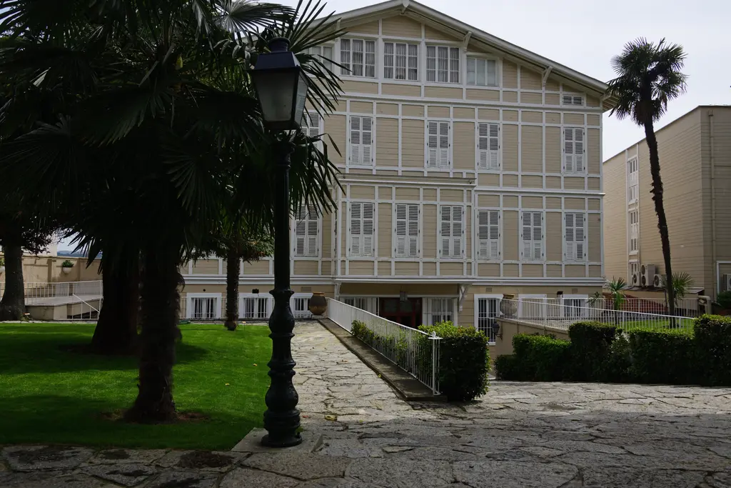 Büyükdere'de Sadberk Hanım Müzesi; açık renk ahşap kaplamalı yalı cephesi, palmiyeler, çimenlik ve taş yol.