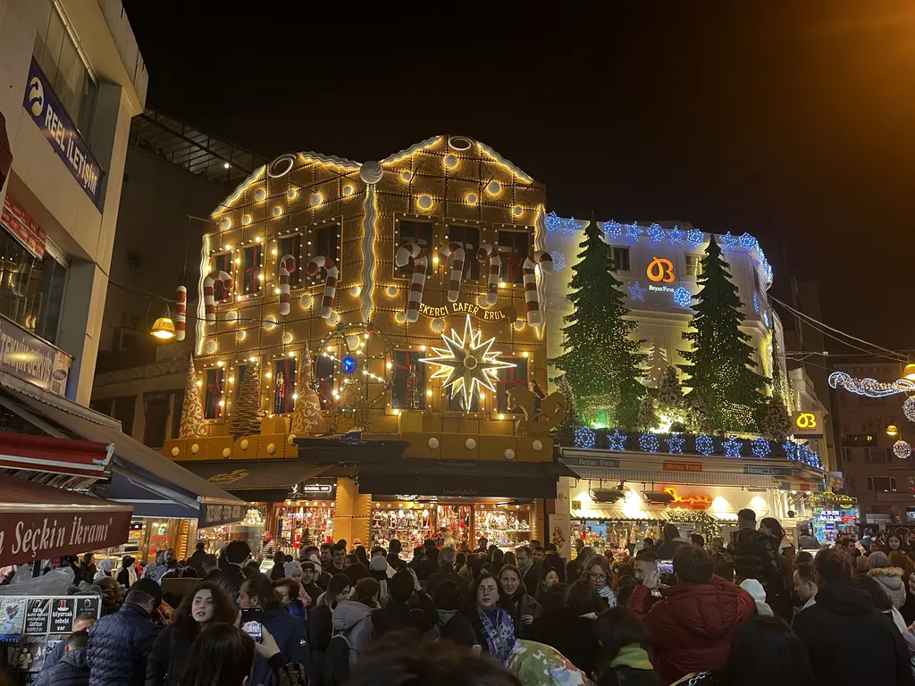Kadıköy Çarşısı'nda gece; yılbaşı ışıklarıyla kaplı şekerci cephesi, çam ağaçları ve sokakta kalabalık.