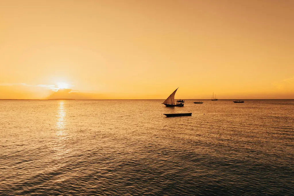 Zanzibar'da geleneksel dhow teknesi; üçgen yelkeniyle turkuaz denizde süzülen ahşap yelkenli.