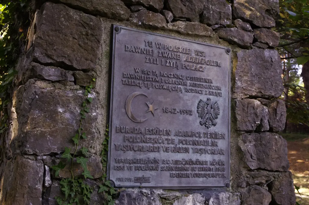 Polonezköy'de taş duvara gömülü bronz plaket; üstte Lehçe yazı, ortada ay yıldız ile Polonya kartalı arasında 1842-1992 tarihi ve altında Türkçe metin.