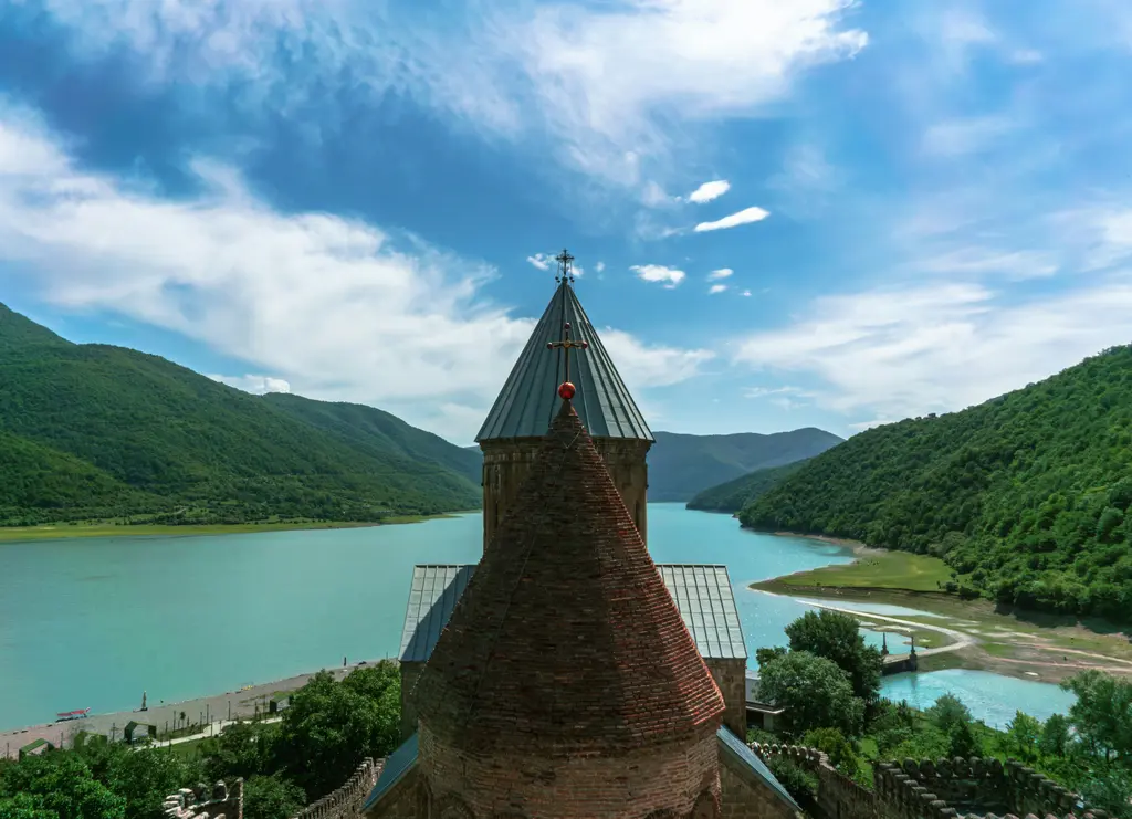 Aragvi rezervuarının kıyısında Ananuri kale-kilise kompleksi; taş surlar, kuleler ve turkuaz su.