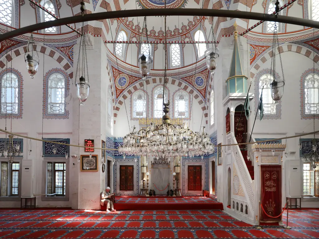 Atik Valide Camii'nin içi; kırmızı halılar, büyük avize, mihrap, minber ve sıra sıra pencereler.