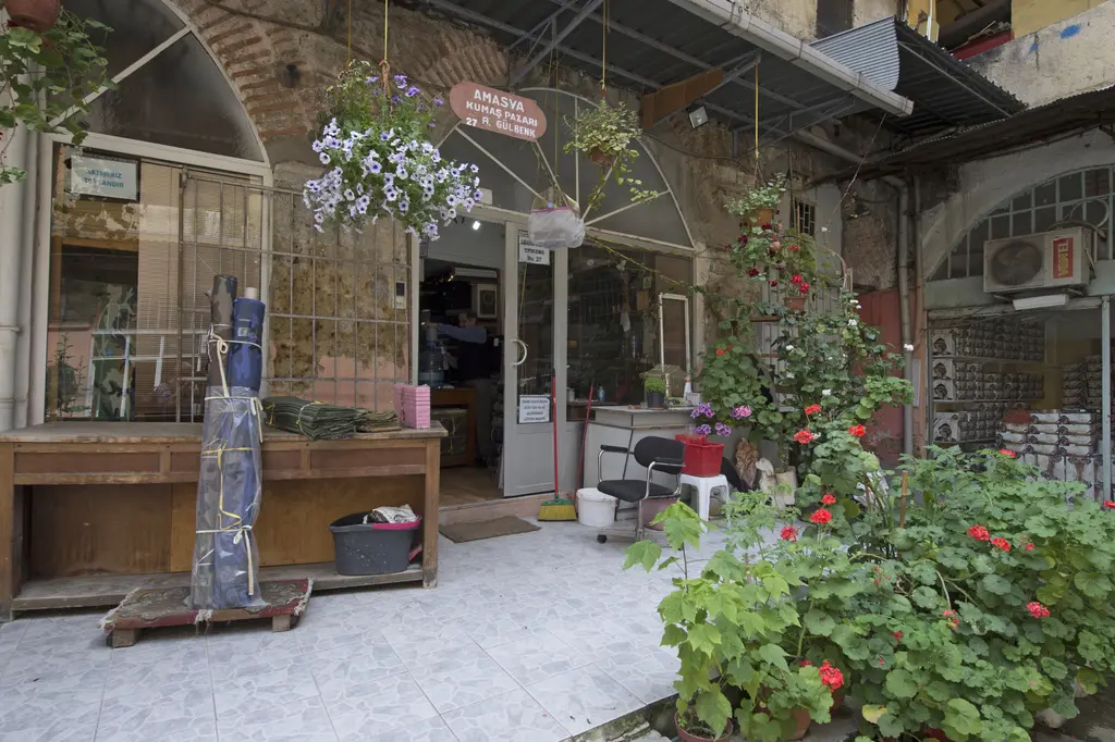 Büyük Yeni Han'da bir kumaş dükkânının önü; tezgâh, asma saksılar, çiçek açmış sardunyalar ve dükkân tabelası.