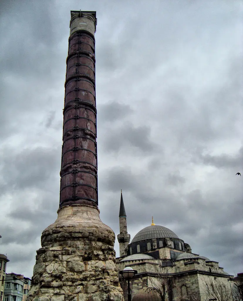 Çemberlitaş'ta fırtına öncesi gökyüzü; koyu bulutların önünde sütun, sağda cami kubbesiyle minare ve altta çatılar.