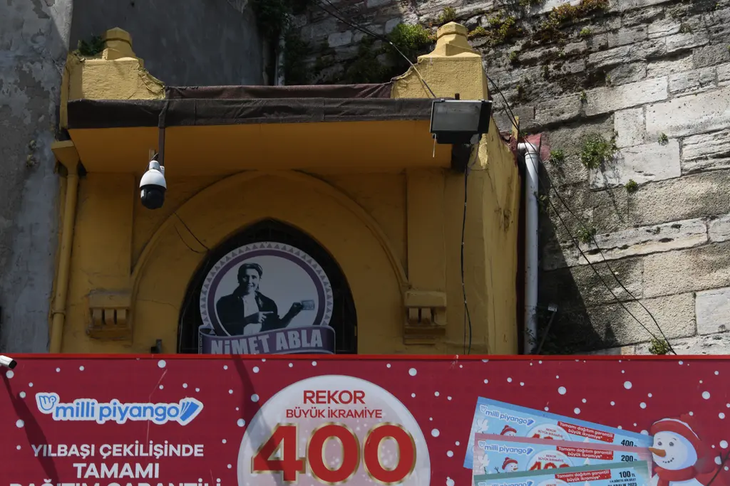 Eminönü'nde Nimet Abla piyango gişesi; sarı boyalı kemerli gişe, tabela, kırmızı ikramiye afişi ve taş duvar.