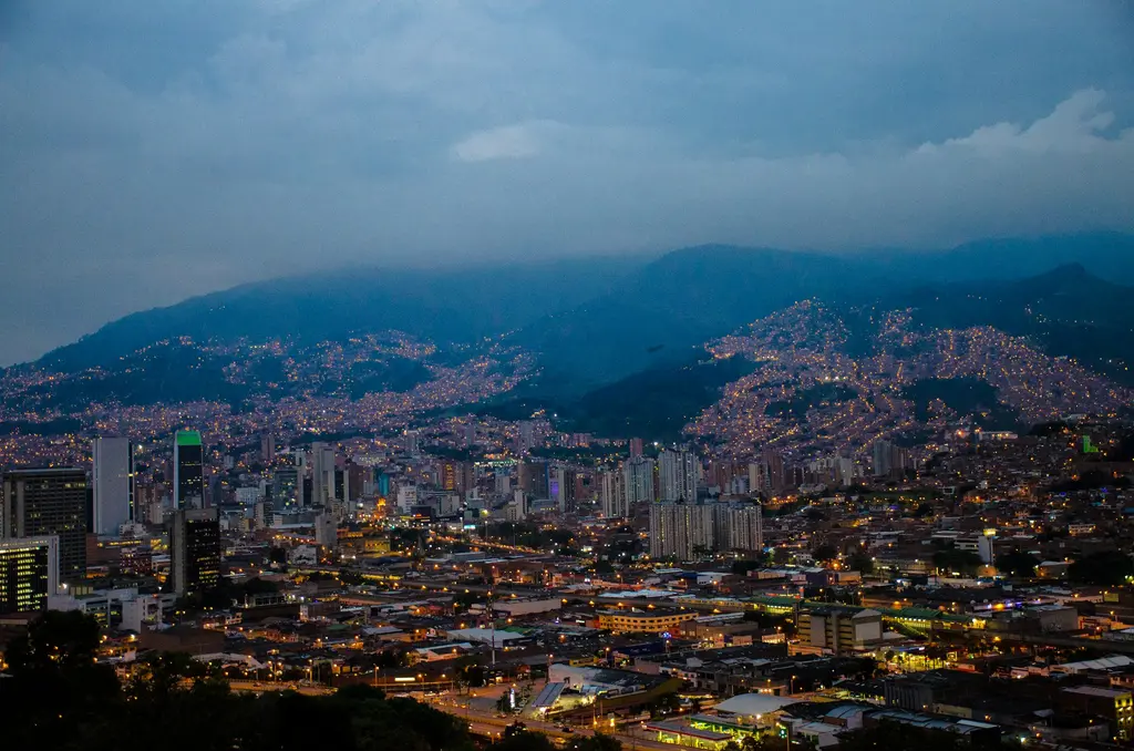 Kolombiya'da Medellín akşam alacakaranlığında; vadiyi ve çevre tepeleri dolduran binlerce ışık, gökdelenler ve bulutlarla örtülü dağlar.